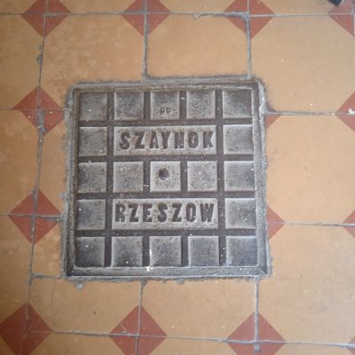 Prostokątny właz wyprodukowany w fabryce J&oacute;zefa Szaynoka, znajdujący się na parterze kamienicy przy Plac Śreniawit&oacute;w 2. Ze zbior&oacute;w Biura Miejskiego Konserwatora Zabytk&oacute;w